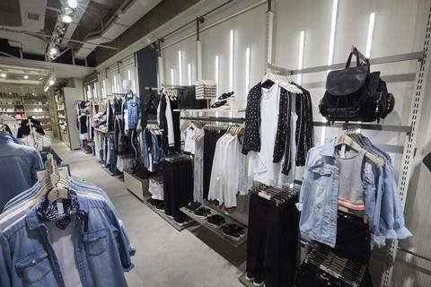 The ground-floor perimeter uses a triple-hanging merchandising system, backed by vertical white-neon lighting